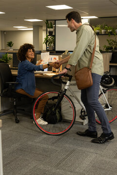 Shaking hands Diverse coworkers exchanging printed charts at office desk with bicycle and plants