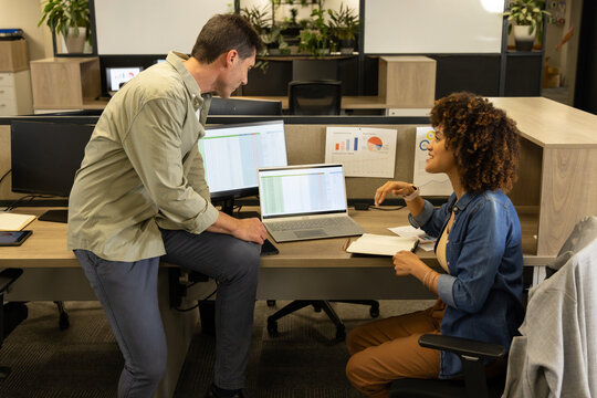 Working Diverse coworkers analyzing spreadsheet data on laptop at modern office, with paper charts