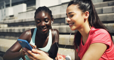 Sports, earphones and girl friends outdoor with phone for listening to music, networking or social media. Laughing, fitness and female athletes on break streaming playlist on mobile app on stairs.
