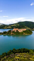 Hillside village nestled on a lake island, surrounded by rolling hills and vibrant greenery under a clear blue sky