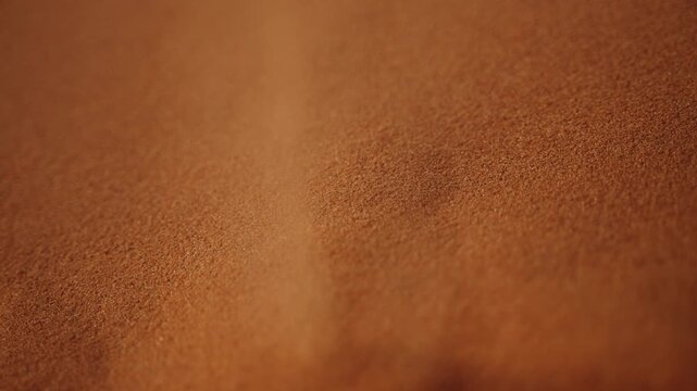 Macro shot of fine desert sand grains cascading in slow motion, capturing delicate texture and movement.