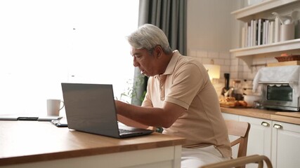 Senior business man working on laptop while checking at document at home. Middle aged manager writing report and looking at financial chart by using computer while sitting at living room. Myrmidon. - Powered by Adobe