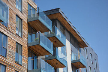 Modern apartment building with wooden accents and glass balconies under clear blue sky.