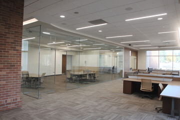 Fototapeta premium Modern office space with glass-walled conference rooms, desks, office chairs, and carpet flooring.