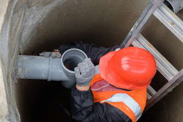 Worker in protective gear installing and inspecting septic system pipes inside a manhole at a private house, ensuring proper drainage, maintenance, and local wastewater management