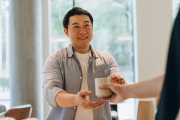 Smiling asian man passing a cup to colleague in office break room