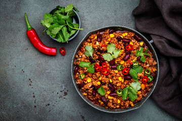 Tex-mex meet chili con carne with beef, red beans,, sweet corn, cilantro in frying pan, rusty green background top view