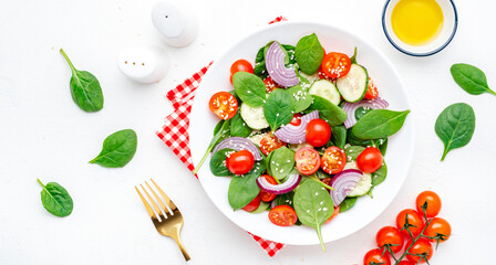 Healthy vegan vegetable salad with spinach, tomatoes, cucumber, onion, sesame seeds and olive oil. White table background, top view