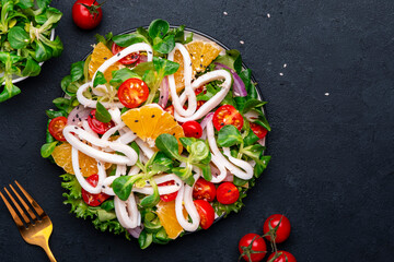 Yummy seafood salad with oranges, squid, tomatoes, lettuce and lemon dressing, black table, top view