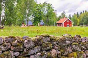 Mossy stone wall with a red cottage in a rural landscape © Lars Johansson