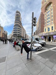 Playful moment from Urban Explorer: A man leans playfully against a lamppost, posing in front of a historic building on Gran Vía in Madrid.
