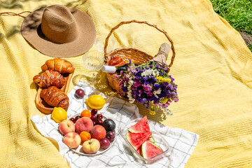 A bright summery picnic setup with fresh fruits, pastries, a floral bouquet, and a wicker basket. Chic glasses and a cozy blanket. Relaxation, enjoying nature, outdoor dining, summer leisure concept