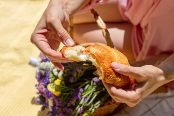 A close-up of a person holding a croissant surrounded by a beautiful picnic setting. A bouquet of colorful fresh flowers creating a cozy outdoor atmosphere. Relaxation, enjoyment, and nature