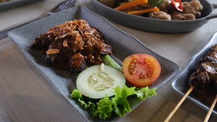 Close-up of plant-based mushroom rendang served with fresh cucumber, tomato, and lettuce on a dark rectangular plate.
