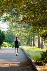 Woman jogging on a tree-lined park path in summer morning light