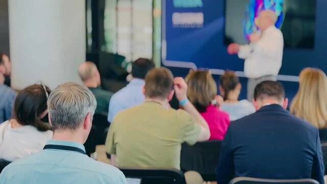 Formal presentation event with speaker addressing audience in modern business setting. Education and professional knowledge exchange atmosphere.