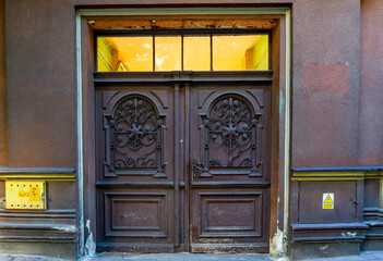Decorative wooden entrance door with metal ornaments in a historic tenement, visible gas and electrical installation signs.