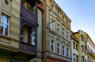 Obraz premium Facade of townhouses with wooden balcony, decorative cornices, and pastel facade in city center, 19th-century architecture, sunny day view, historic urban buildings