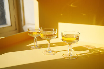 Three champagne coupe glasses filled with golden liquid clear glass stemmed glasses