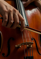 A close-up shot highlights the hands of a musician expertly drawing the bow across the strings of a cello, capturing the intricate details of their performance