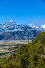 Obraz premium Majestic snow-covered peaks rise above a golden valley bordered by green forest.