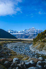 Clear stream flows through a rocky valley with snow-covered peaks in the distance.