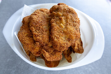 Golden fried pork cutlets in white bowl on gray countertop