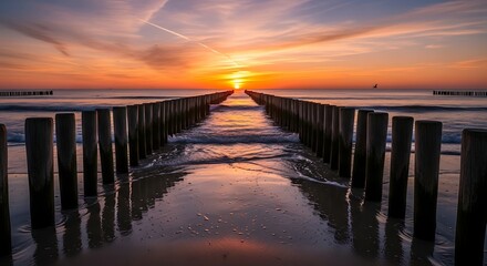 Obraz premium Serene seascape at sunset featuring wooden posts leading towards the horizon