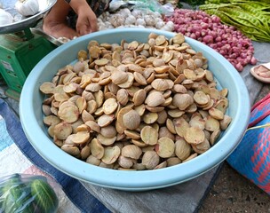 A bowl full of jengkol slices at a market stall, surrounded by other fresh produce.