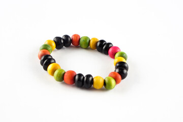 A colorful wooden bead bracelet lies on a white surface. The bracelet is made up of black, green, yellow, and red beads.