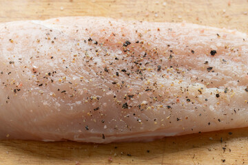 Close-up of raw chicken breast with salt and black pepper on wood