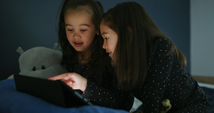 Bonding, tablet and children in bedroom for movie, film or video on app for entertainment together. Relax, night and sisters watching show on streaming website with digital technology in home.
