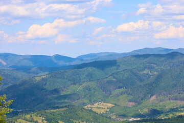 Fototapeta premium Endless wooded mountain ranges stretching into the distance create a breathtaking panorama. Small villages are nestled among them, surrounded by greenery, and above this majestic landscape, a blue sky