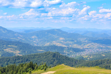 Obraz premium Endless wooded mountains stretching into the distance create a breathtaking panorama. Between them, in the valley, lies a picturesque mountain village, and above this majestic landscape, a blue sky wi