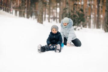 Happy children playing with sled in snowy forest during winter day
