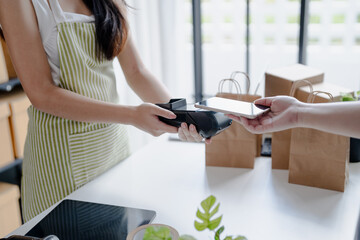 Asian Woman Using Mobile Phone for Contactless Payment with POS at Small Business