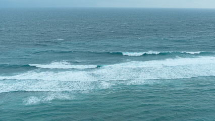 Waves roll across the turquoise ocean under a cloudy sky, creating a serene and refreshing seascape full of movement and natural beauty.