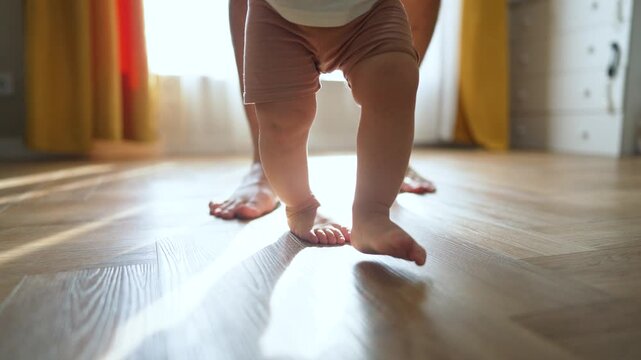 Father helps take first step. Son learning to walk with father guidance. Proud father supports son first walk indoors. Son takes first step while walking with. Father teaches son to step and walk.