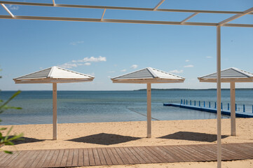 Modern beachfront gazebo with umbrellas and pier on sandy shoreline