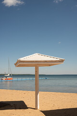 Sunny beach scene with umbrella and sailboat under clear blue sky