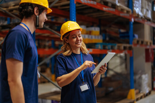 Female warehouse worker holding a tablet and talking to her coworker - Powered by Adobe