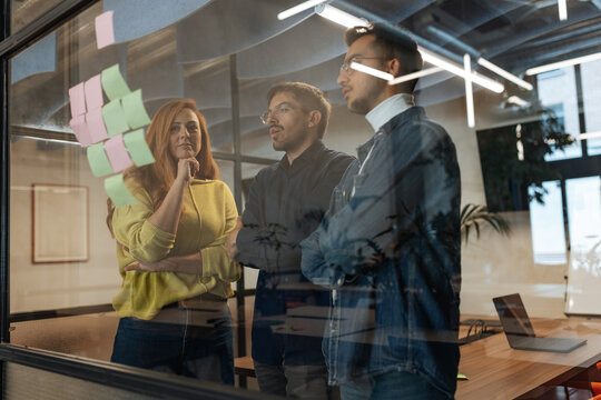 Businesspeople brainstorming using sticky notes on glass wall in office