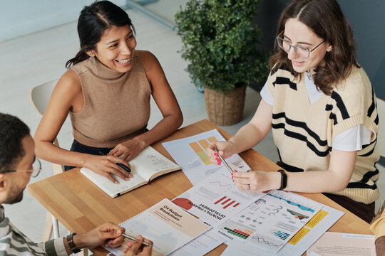 Young businesswoman in eyeglasses presenting her financial report to colleagues at table during business meeting