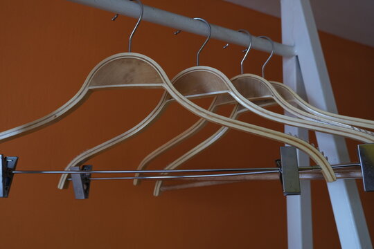Several wooden hangers neatly arranged on a metal clothing rack against an orange wall, symbolizing minimalism or wardrobe organization.
