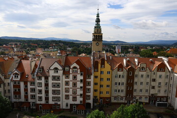 Obraz premium Colorful residential buildings and historic town hall tower in Kłodzko, Poland, with mountain landscape in the background