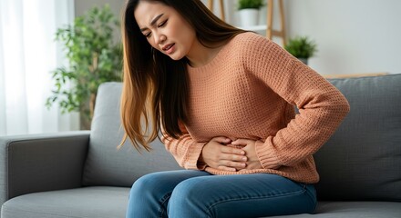 Young Asian woman experiencing stomach pain while sitting on a sofa at home