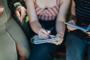 Students writing in notebooks while seated outdoors, engaging in collaborative learning in a natural setting.