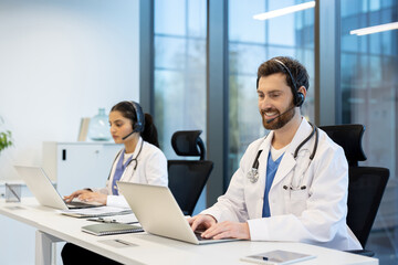 Two doctors wearing headsets and utilizing laptops in a bright and contemporary workspace, emphasizing communication and technology in healthcare.
