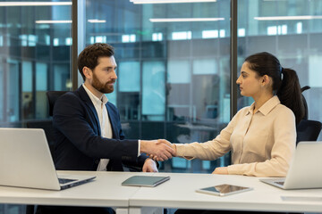 Business professionals engage in a formal handshake at a modern workplace, symbolizing agreement.