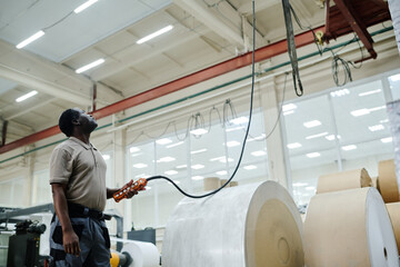 Mature African American man working in print shop warehouse holding controller using lifting gear
